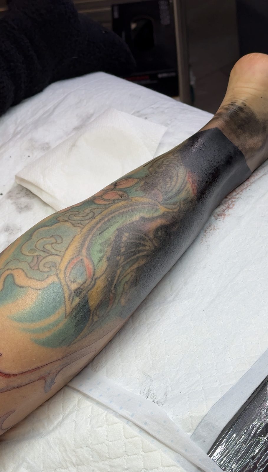 Blackwork cover-up in progress over an old colour leg tattoo, by Si, Bristol